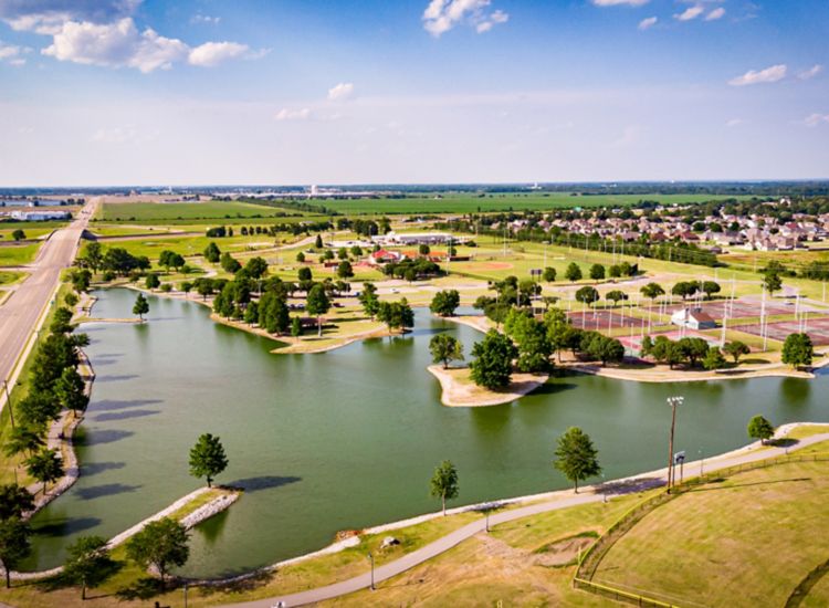 Aerial view of a park with a pond and several sports fields on a sunny day.