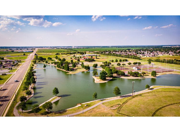 Aerial view of a park with a pond and several sports fields on a sunny day.