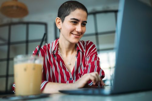 Young woman on laptop with iced coffee in foreground.