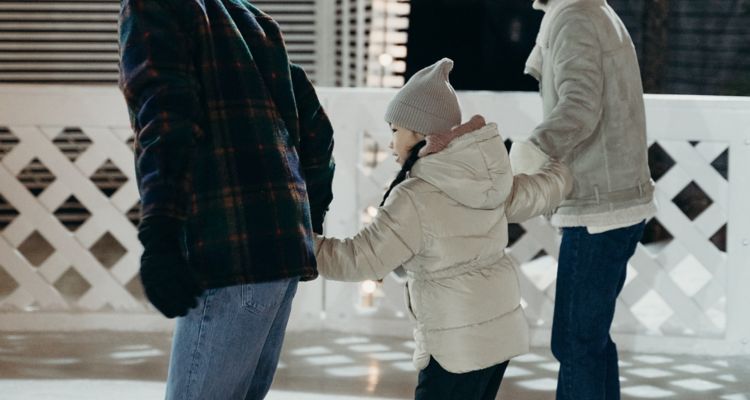 Family holding hands and ice skating on a rink at night.