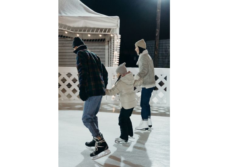 Family holding hands and ice skating on a rink at night.