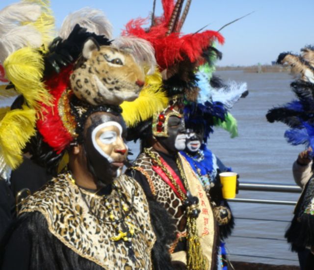 Zulu Krewe members wearing feather headdresses and animal print walking along a river.