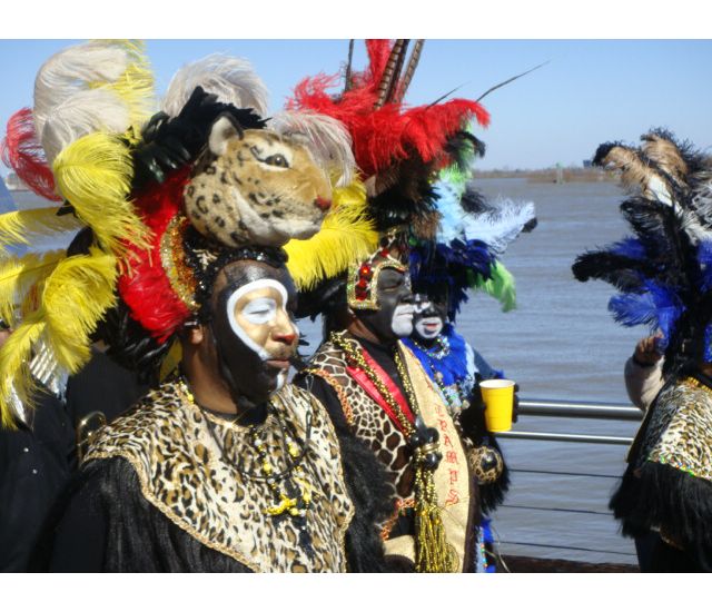 Zulu Krewe members wearing feather headdresses and animal print walking along a river.