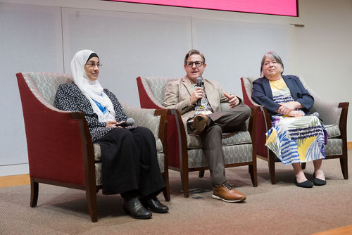 three people sitting in chairs on a stage.