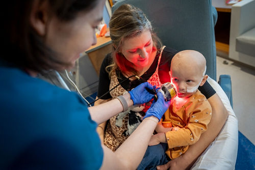 A patient receiving photobiomodulation therapy while sitting in her mother's lap.