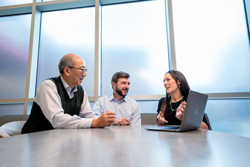Three people sitting at a table in front of a laptop