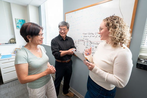 Two women and a man talking in front of a whiteboard.