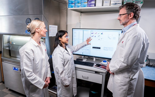 Two women and a man in a lab. One woman is explaining something on a computer screen.