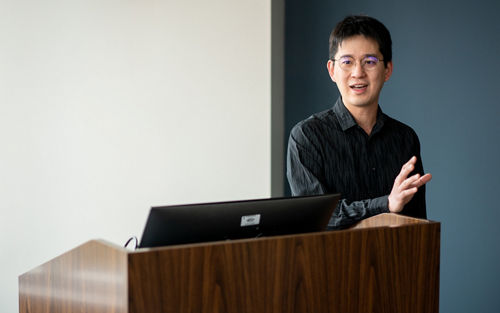Imnage of Chi-:Lun Chang, in black shirt, standing at podium