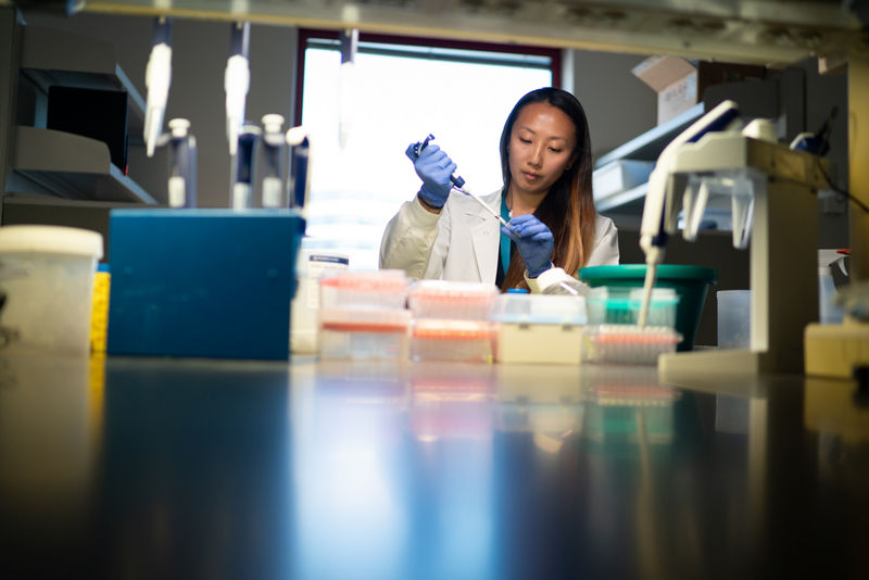 A scientist in a lab coat sitting at a research bench holding a pipette
