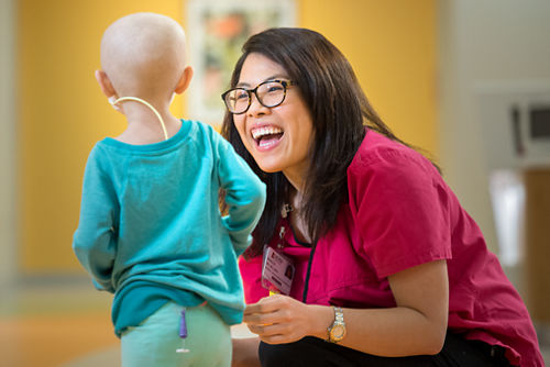 Smiling nurse stooped and interacting with very young cancer patient.