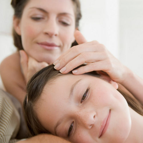 Mother gently stroking daughter's hair while child rests peacefully, nurturing parent-child moment showing care and comfort in home setting