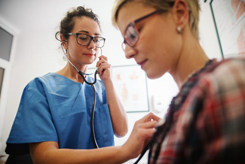 Female doctor listening to female patient's heart with stethoscope