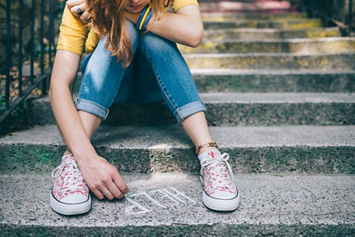 Una adolescente escribe “Help” (Ayuda) con tiza en el suelo.