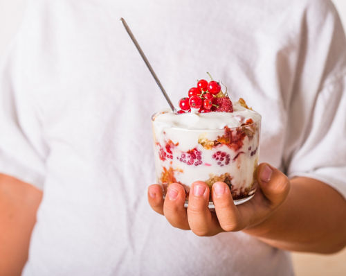 Closeup of hand holding a large cup of yogurt and fruit parfait.