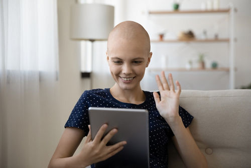 Young woman with cancer chatting with friends on video call holding tablet