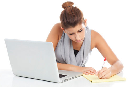 Student working on computer and writing in notebook
