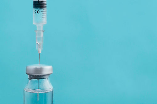 Foto de la aguja de una jeringa que extrae el medicamento de un vial de vidrio