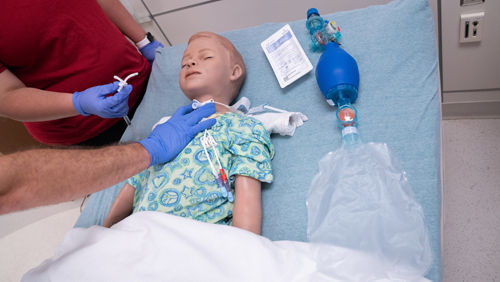 Un cuidador principal practica la colocación correcta de las manos para una traqueotomía con un maniquí