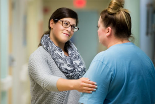 Woman touching another woman's arm reassuringly within a clinical setting.