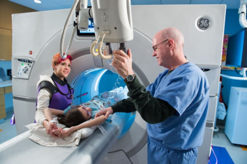 CT technologist administers contrast to a pediatric cancer patient with her mom nearby.