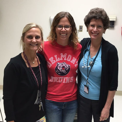 A cancer survivor standing with two members of a care team in an examination room.